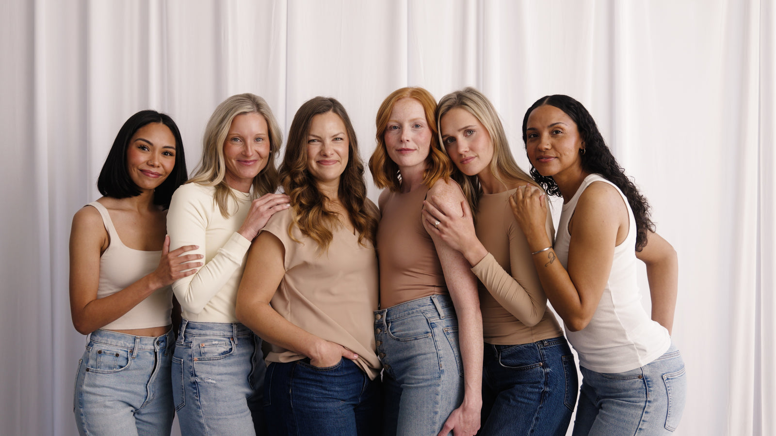 Six women standing together in front of a soft white curtain